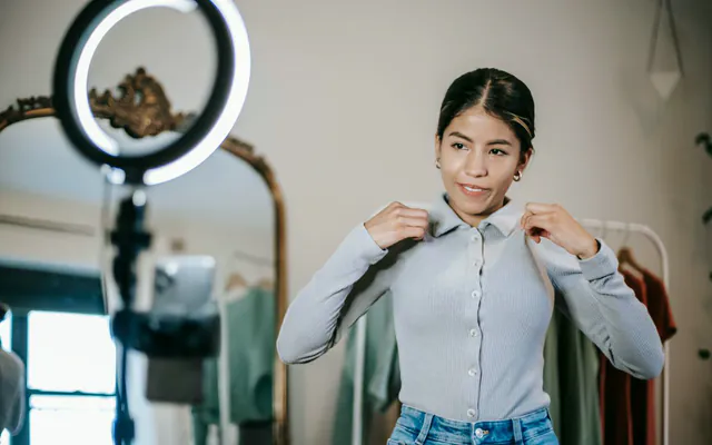 Criadora de conteúdo experimenta roupas diante de um ring light e de um telefone