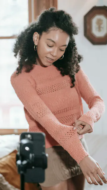 Creator showing a knit sweater to a phone on a tripod